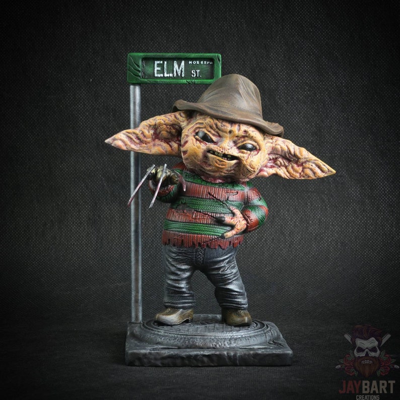 May include: A small, green street sign reads "ELM ST."  A small, brown, and green figure with large ears and a brown hat stands on a gray base. The figure is wearing a red and green striped shirt, blue jeans, and brown shoes. The figure has a menacing expression and is holding a pair of sharp, silver claws.
