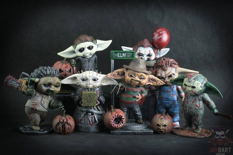 May include: A collection of eight horror movie character figurines, each with a unique design and paint scheme. The figurines are all in the style of the popular "Baby Yoda" character, with large ears and big eyes. The characters include Freddy Krueger, Jason Voorhees, Chucky, Pennywise, Leatherface, Michael Myers, and two others. The figurines are all standing on a black surface with a few pumpkins in front of them.