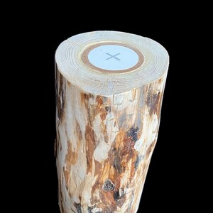 Puede incluir: Un portavelas de tronco de madera con un centro blanco y un diseño de cruz. El tronco tiene un patrón de veta de madera natural con tonos marrones y blancos.