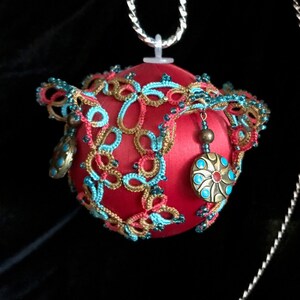 May include: A red satin Christmas ornament with gold and turquoise crocheted lace and decorative metal accents.