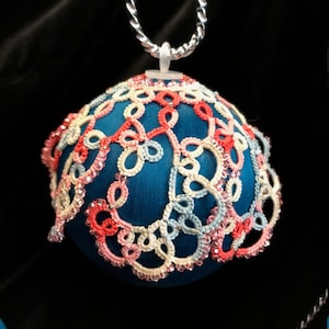 May include: A teal blue Christmas ornament with a delicate lace design in pink, white, and light blue. The lace is beaded with small, clear beads.