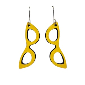 May include: A pair of yellow wooden earrings in the shape of eyeglasses. The earrings have a black outline and silver-colored ear wires. The design is modern and minimalist.