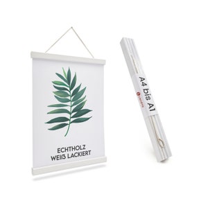 Könnte beinhalten: Weißer Holzposterrahmen mit einem grünen Blattdesign und dem Text "ECHTHOLZ WEISS LACKIERT". Der Rahmen hängt an einer weißen Wand. A4 bis A1 steht auf der weißen Verpackung.