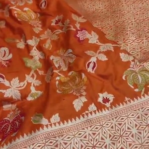 Puede incluir: Un sari de seda de color óxido con un patrón floral y un borde plateado. El borde presenta un diseño geométrico con un patrón repetitivo de estrellas.