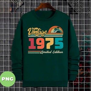 Puede incluir: Una camiseta de manga larga verde oscuro con un dise&ntilde;o vintage de 1975. La camiseta tiene un gr&aacute;fico de colores arco&iacute;ris con palmeras y el texto "Vintage 1975 Limited Edition".