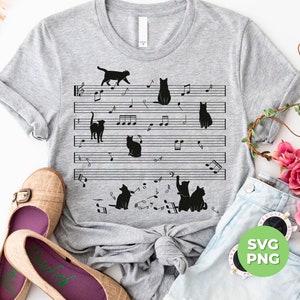 Könnte beinhalten: Ein graues T-Shirt mit einem Design aus schwarzen Katzen auf einem Notenblatt mit Noten. Das Design zeigt mehrere Katzen in verschiedenen Posen, darunter sitzend, stehend und Musik spielend. Das T-Shirt ist ein tolles Geschenk für Katzenliebhaber und Musikbegeisterte.