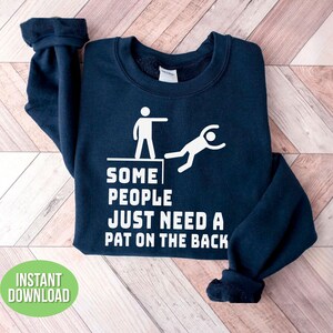 Pu&ograve; includere: Felpa blu navy con grafica bianca di due omini stilizzati e la scritta "SOME PEOPLE JUST NEED A PAT ON THE BACK." Un cerchio verde con le parole "INSTANT DOWNLOAD" si trova in basso a sinistra.