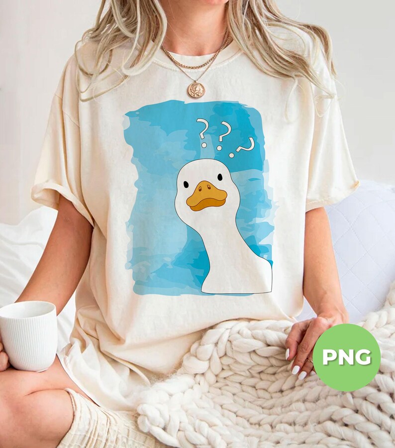 May include: A white t-shirt with a blue watercolor background and a cartoon goose with question marks above its head. The text on the shirt reads '???'.