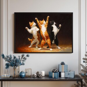May include: A framed artwork depicts three cats in a dancing pose. The cats are orange and white, orange tabby, and black and white. The background is dark, and the cats are in a spotlight. The artwork is displayed above a table with holiday decorations.