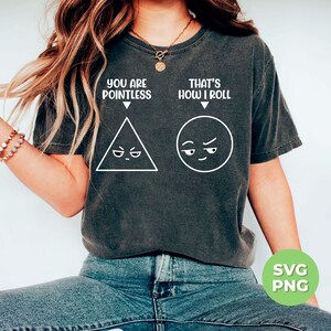 May include: A dark gray t-shirt with a white graphic design. The graphic features a triangle with a frowning face and a circle with a smirking face. The text "You are Pointless" is above the triangle and "That's How I Roll" is above the circle.