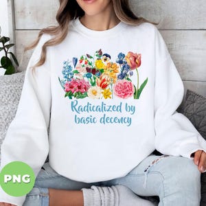 Può includere: Felpa bianca con un design floreale colorato e la scritta "Radicalized by basic decency" in azzurro. La composizione floreale comprende fiori rosa, gialli, rossi e blu. La felpa è di stile casual.