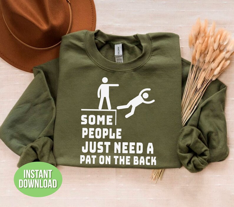 Pu&ograve; includere: Una felpa verde oliva con testo e grafica bianchi. Il testo recita "SOME PEOPLE JUST NEED A PAT ON THE BACK." Una grafica bianca raffigura una persona che ne spinge un'altra da una sporgenza. Le parole "INSTANT DOWNLOAD" sono in un cerchio verde.