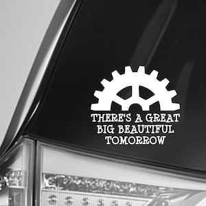 May include: White vinyl decal featuring a gear design and the text "THERE'S A GREAT BIG BEAUTIFUL TOMORROW." The decal is applied to a black vehicle surface, likely a car window or body panel.