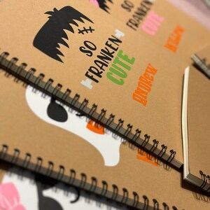 Puede incluir: Cuadernos de papel kraft con encuadernaci&oacute;n de alambre negro. Las cubiertas presentan dise&ntilde;os tem&aacute;ticos de Halloween, incluyendo un monstruo de Frankenstein con el texto "So Franken Cute" y un fantasma con un lazo rosa. El nombre "Andrew" tambi&eacute;n est&aacute; impreso.