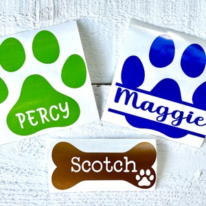 May include: Three dog paw print stickers with names Percy, Maggie, and Scotch. The paw prints are green, blue, and brown.