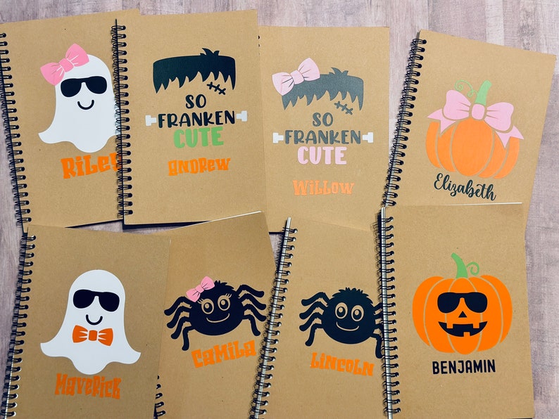 Puede incluir: Una colecci&oacute;n de cuadernos con espiral con dise&ntilde;os de Halloween. Cada cuaderno presenta un gr&aacute;fico diferente, incluyendo un fantasma, Frankenstein, una ara&ntilde;a y una calabaza, con nombres personalizados en naranja o negro.