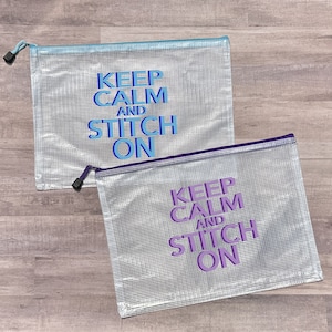 May include: Two clear plastic zippered bags with mesh fabric. The bags have the text "Keep Calm and Stitch On" printed in blue and purple on a silver background.