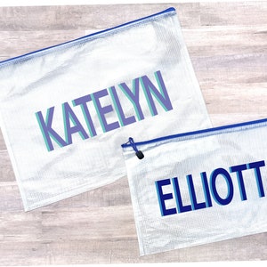 May include: Two clear mesh zippered bags with blue trim. The larger bag has the name "KATELYN" printed in purple and teal. The smaller bag has the name "ELLIOTT" printed in blue.