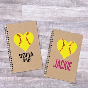 May include: Two brown spiral notebooks with a yellow softball heart design. One notebook says "Sofia #12" and the other says "Jackie".