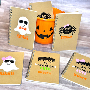 Puede incluir: Una colecci&oacute;n de cuadernos con espiral con dise&ntilde;os de Halloween. Los cuadernos presentan ilustraciones de fantasmas, ara&ntilde;as y el monstruo de Frankenstein, junto con nombres como Maverick, Camila, Riley, Andrew y Willow. Tambi&eacute;n hay un cubo de calabaza naranja.