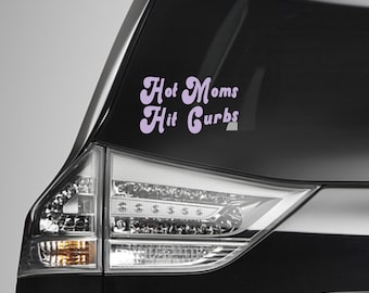 May include: A light purple vinyl decal applied to a car window featuring the text Hot Moms Hit Curbs in a bold, retro-inspired font. The sticker is positioned on the rear glass of a black vehicle, displaying the phrase in two distinct lines.