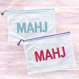May include: Two clear plastic zippered pouches with the word "MAHJ" printed on them. The top pouch has the word printed in teal and the bottom pouch has the word printed in pink and orange.