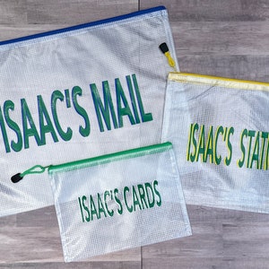 May include: Three clear mesh zippered bags with green and blue lettering. The largest bag says "ISAAC'S MAIL", the medium bag says "ISAAC'S STATIONARY", and the smallest bag says "ISAAC'S CARDS".