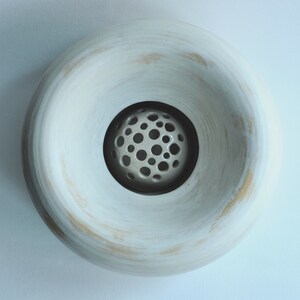 May include: White ceramic bowl with a round, open top and a smaller, round, perforated bowl inside. The bowl has a slightly textured surface.