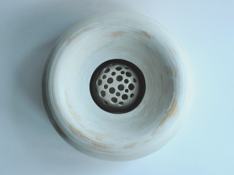May include: White ceramic bowl with a round, open top and a smaller, round, perforated bowl inside. The bowl has a slightly textured surface.