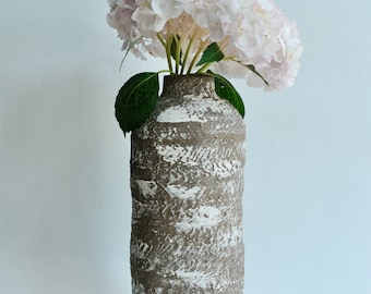 Può includere: Un vaso in ceramica bianco e marrone con una superficie testurizzata contiene un mazzo di ortensie rosa pallido.