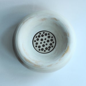 May include: White ceramic bowl with a round, slightly raised rim and a circular metal grate with small holes in the center.