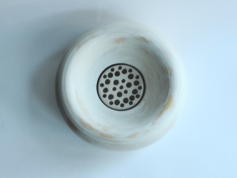 May include: White ceramic bowl with a round, slightly raised rim and a circular metal grate with small holes in the center.