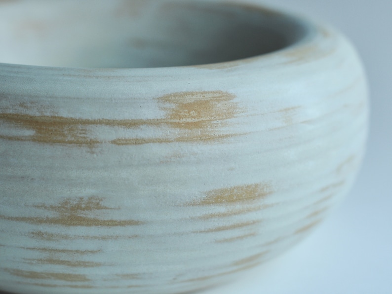 May include: A white ceramic bowl with a light brown glaze. The glaze has a streaky, textured appearance.
