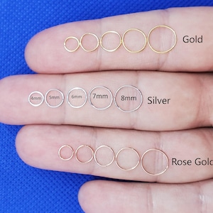 May include: A hand displays three sets of hoop earrings in gold, silver, and rose gold. The gold hoops range in size, and the silver hoops are labeled 4mm to 8mm. The rose gold hoops are also displayed. The text "Gold", "Silver", and "Rose Gold" are included.