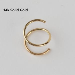 May include: A 14k solid gold spiral earring. The earring is a continuous, curved design with a circular shape. The text "14k Solid Gold" is in the upper left corner.