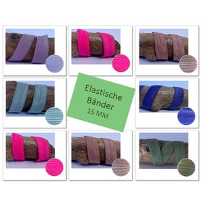 Puede incluir: Una colección de bandas elásticas de 15 mm de ancho en varios colores sólidos, incluyendo lavanda, rosa intenso, beige, azul claro, azul oscuro, rosa brillante, marrón y verde oliva, sobre piezas de madera con una etiqueta verde central Elastische Bänder 15 MM.