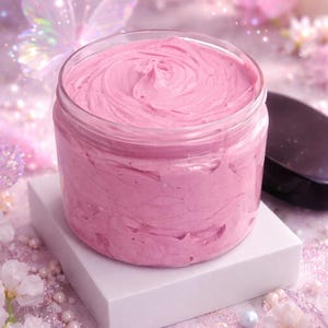 Peut inclure: Un pot de beurre corporel rose sur un cube blanc, dans un décor doux et onirique. Le beurre corporel a une texture tourbillonnée. La scène est ornée de fleurs, de perles et d'un papillon holographique.