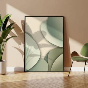 Könnte beinhalten: Abstrakter Kunstdruck in einem schwarzen Rahmen. Das Kunstwerk zeigt überlappende, abgerundete Formen in Grün- und Beigetönen. Der Druck wird an einer Wand mit einer Pflanze und einem Stuhl im Hintergrund ausgestellt, was eine moderne Ästhetik schafft.