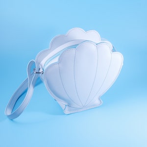 May include: A light blue faux leather handbag shaped like a seashell with a matching strap.
