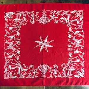 May include: Red cotton bandana with a white star in the center and a white border design of stylized figures and bells. The design is reminiscent of a Christmas carol.