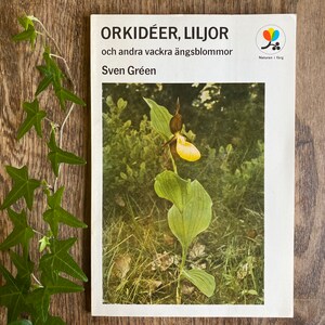 May include: A book cover with the title "ORKIDÉER, LILJOR" and the subtitle "och andra vackra ängsblommor" by Sven Gréen. The cover features a yellow and brown orchid flower.