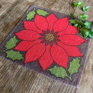 May include: A brown fabric placemat with a red poinsettia flower design. The flower has green leaves and a brown center.