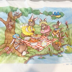 May include: A white fabric panel featuring a printed illustration of rabbits having a picnic by a pond. The scene includes a red and white checkered blanket, a tree with an owl and mouse, a frog, and text reading 1753 F ©the creative circle 198