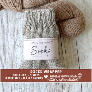 May include: A pair of gray knitted socks with a label that reads "HANDMADE WITH Socks". The socks are wrapped with a brown label that says "SOCKS WRAPPER" and "LETTER SIZE - 11 X 8.5 INCHES". A ball of brown yarn is in the background.