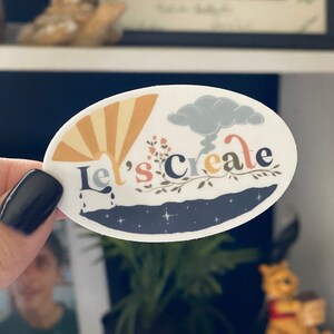 May include: A white sticker featuring a colourful illustration of a sun, clouds, and a branch with leaves. The text "Let's Create" is written in a stylised font.