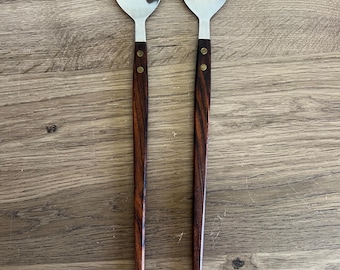 May include: A set of two wooden handled salad serving utensils. The utensils are made of stainless steel and have a dark brown wooden handle with brass accents.