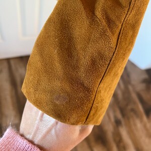 May include: Close-up of the brown suede fabric of a jacket. The fabric has a soft, textured appearance.