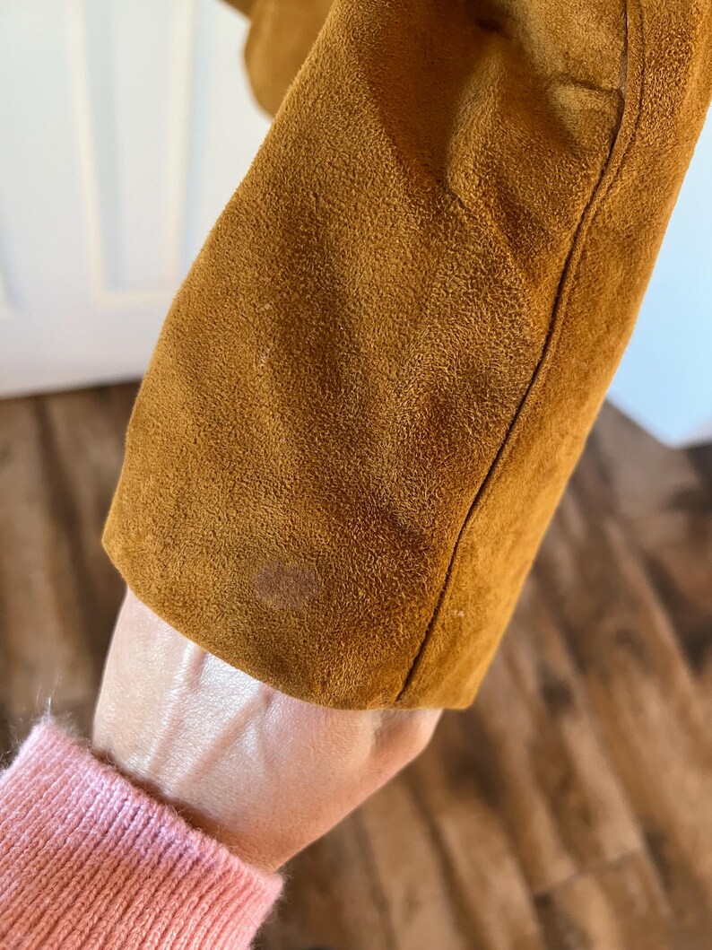 May include: Close-up of the brown suede fabric of a jacket. The fabric has a soft, textured appearance.