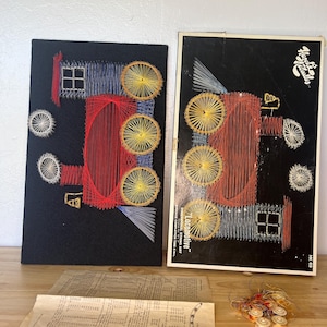 May include: Two vintage string art pieces showing a locomotive on a black background. The string art uses red, yellow, blue, and white thread. The box for the string art is also visible, along with instructions and spools of thread.