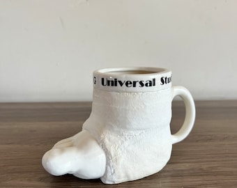 Gli studi universali vintage rompono una tazza per le gambe, un calco e una tazza per i piedi souvenir anni '80 bianco e nero